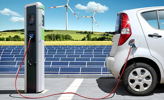 E-Auto an Ladesäule mit Photovoltaik und Windrädern im Hintergrund
