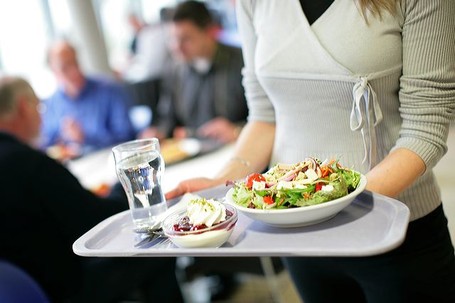 Eine Frau die ein Tablett mit Essen und Trinken in den Händen trägt.